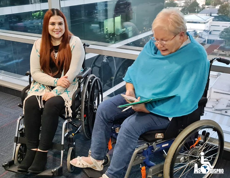 Durante la entrevista, en sus sillas de ruedas, Lucrecia sonríe a cámara, mientras Ulla realiza anotaciones con su teléfono y un folder.