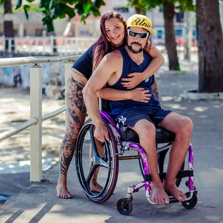 Danielle, un tanto agachada por la silla de ruedas, abraza a Felype mientras él parece ver a la cámara tras sus lentes oscuros.