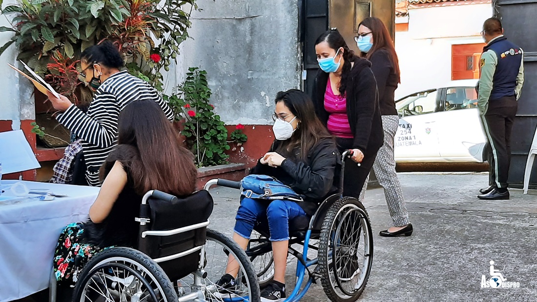 Personas en silla de ruedas y otras personas interactúan usando mascarillas. 