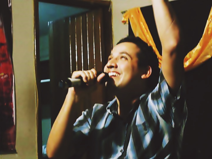 Con una mano en alto y el micrófono en la otra mano, Juanjo sonríe mientras canta. 