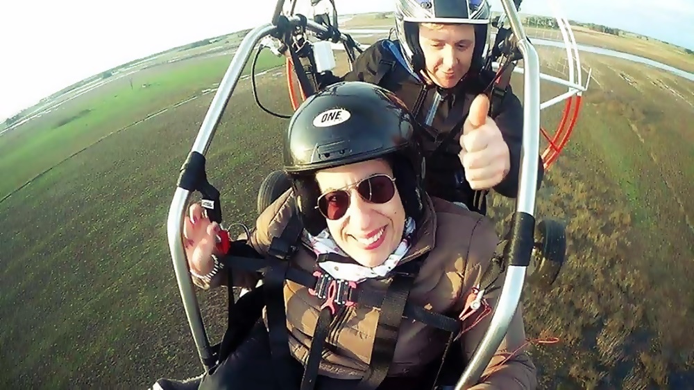 Daiana está volando en parapente junto a su entrenador. Se observa el suelo distante bajo de ellos.