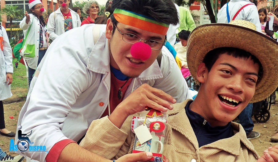 Juan,un joven con parálisis cerebral, recibe un regalo navideño de manos de un voluntario con nariz de payaso. 
