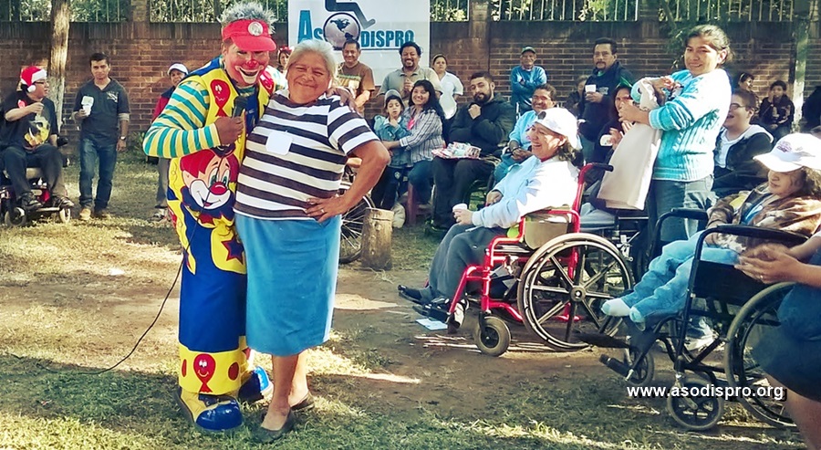 Un payaso posa junto a Doña Marce, mientras muchos participantes sonríen al fondo.