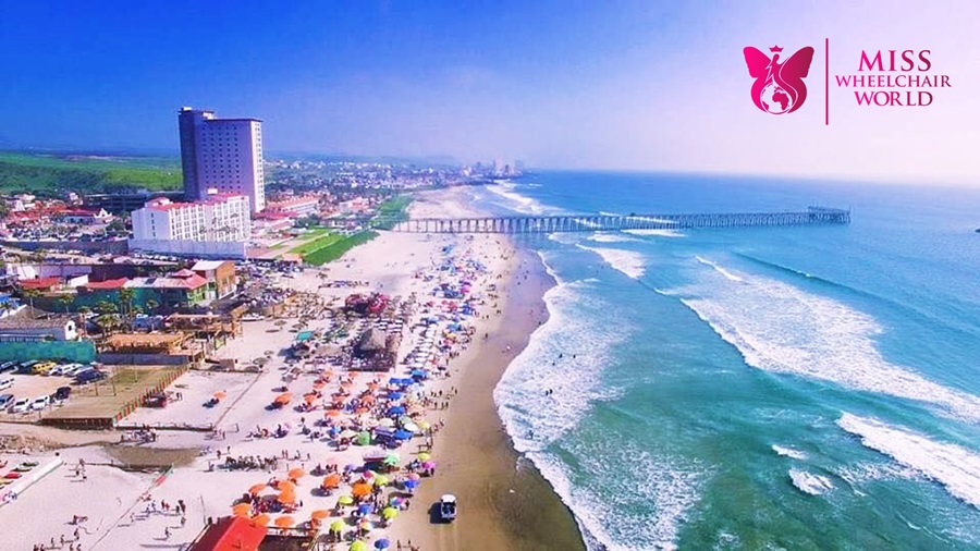 Fotografía panorámica desde el aire, se ven la playa bajo un cielo despejado y muchos vacacionistas. 