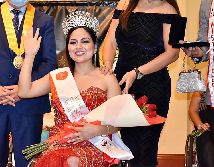 Con un vestido rojo de lentejuelas, su corona y un ramo de flores rojas en una sus manos, Sandy saluda con su otra mano sonriendo.