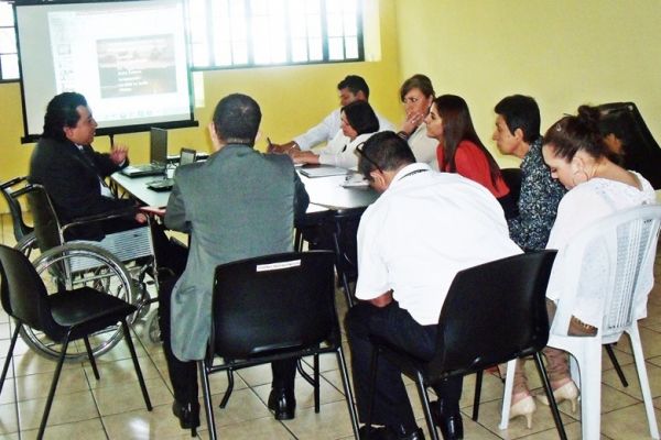 En una mesa de juntas, con una pantalla de presentaciones, Byron Pernilla se dirige a un grupo de ejecutivos.