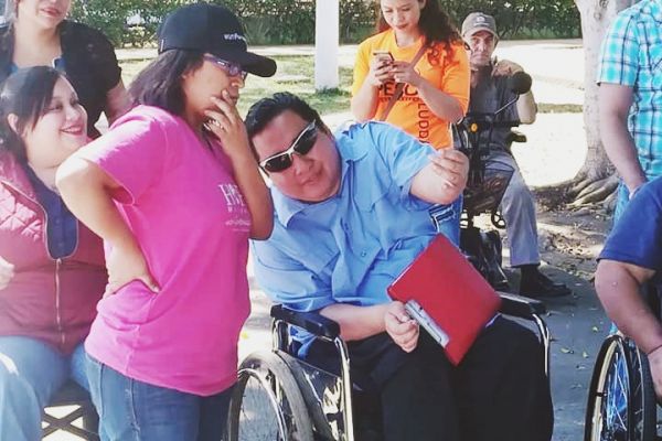 Byron Pernilla en su silla de ruedas dirige junto a una voluntaria sin discapacidad el Paseo Navideño Asodispro, a su alrededor varios voluntarios del evento.