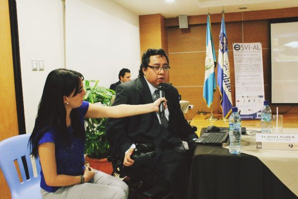 En un auditorio de Universidad Galileo, Byron Pernilla de saco y corbata, se dirige al público mediante un micrófono que sostiene una asistente.