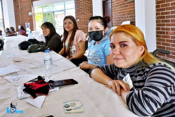 Socias de Asodispro, 4 chicas usuarias de silla de ruedas, ven a cámara en una mesa de trabajo durante el taller.