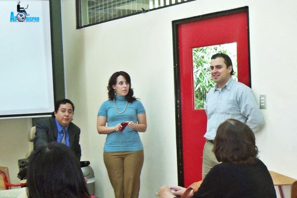 En un aula de Universidad Galileo, Byron, Eimy y Héctor, capacitan a varias personas en sus escritorios.