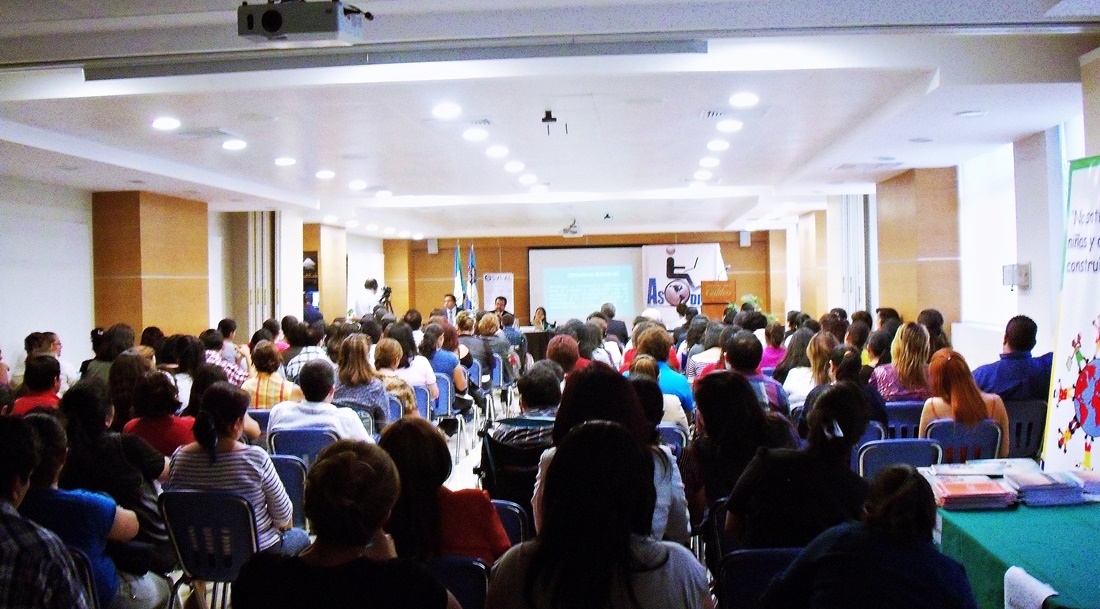 Auditorio de Universidad Galileo lleno, unas 200 personas, al fondo se ve una manta con el logo de ASODISPRO