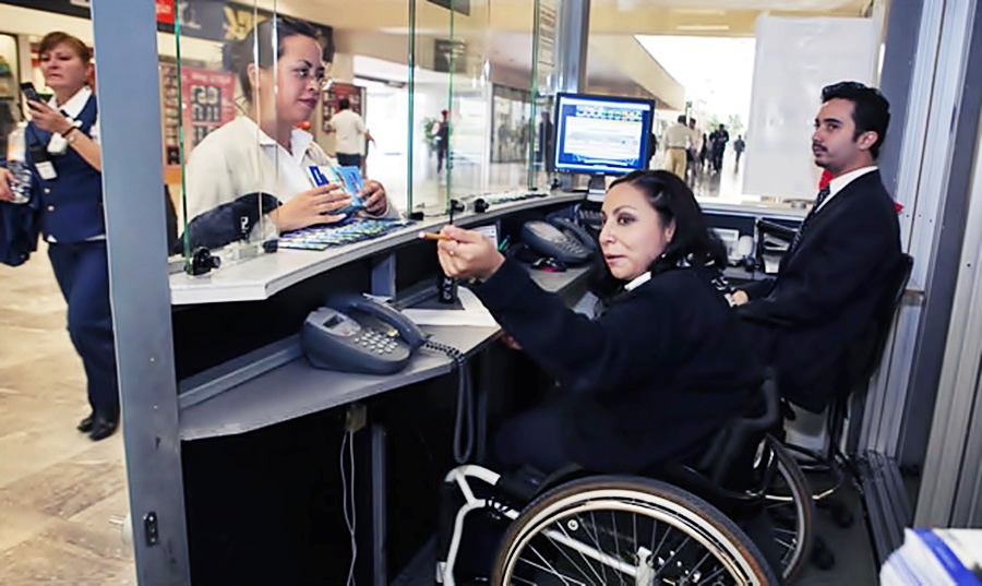 En una recepción, una mujer en silla de ruedas, debidamente uniformada, da indicaciones a un visitante